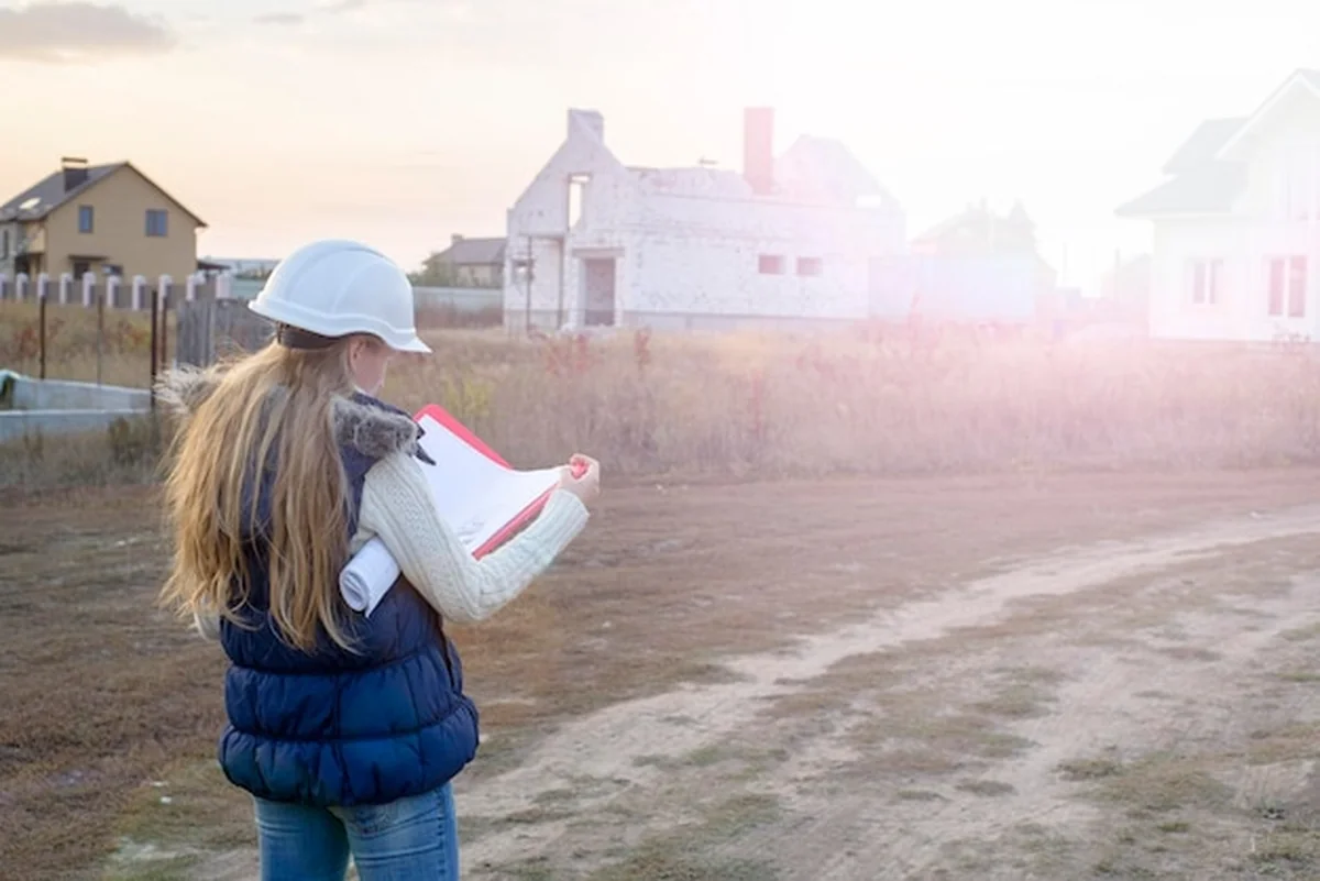 Kobieta w białym kasku z planem w ręku obok budynku