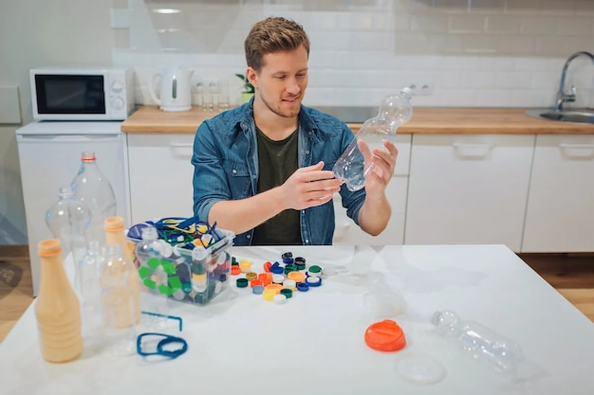 Młody uśmiechnięty mężczyzna sortuje pustą plastikową butelkę obok siedzącego przy stole