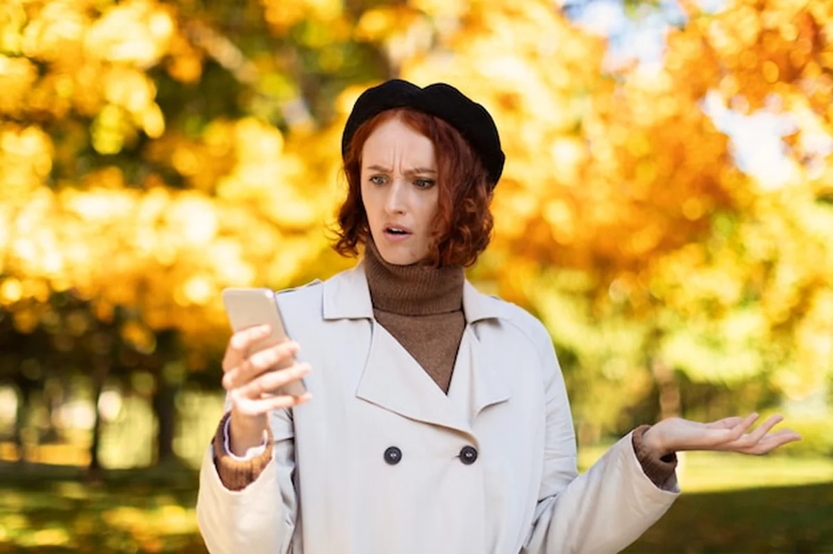 Kaukaska kobieta w płaszczu przeciwdeszczowym patrzy na telefon