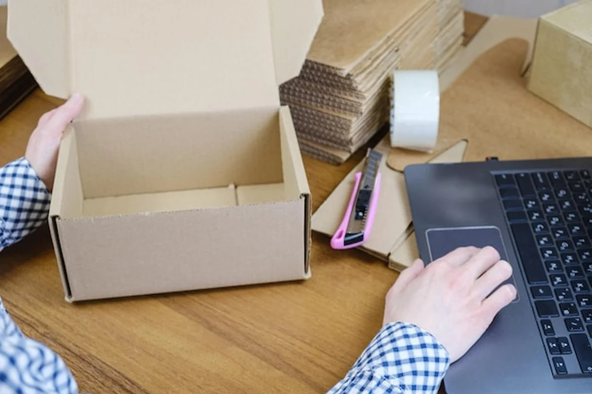 Kobieta przy biurku pakująca zamówienie w kartonowe pudełko